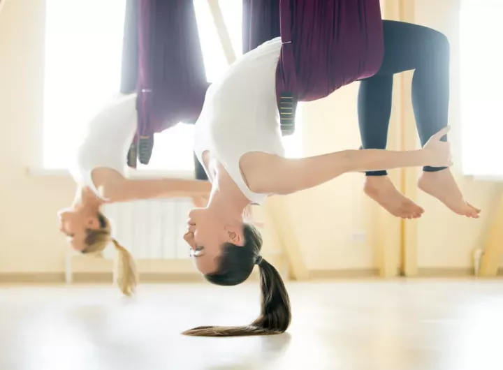 two young women hanging from yoga hammocks