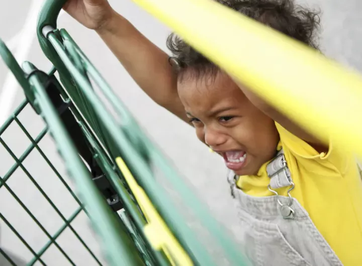 little girl having tantrum while holding on to shopping trolley